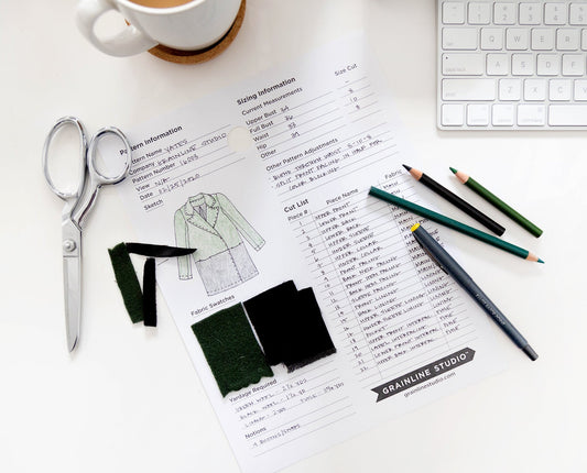 Grainline Studio pattern planning sheet flat lay with dressmaking shears, fabric swatches, colored pencils, mug, and keyboard