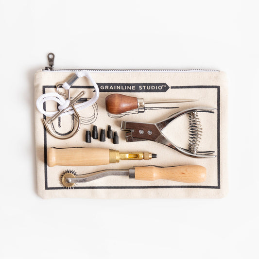 Grainline Studio Pattern Essentials Kit on cream canvas pouch, showing pattern hook, awl, notcher, tracing wheel, and screw punch