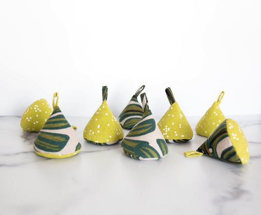 Grainline Pattern Weights sewn in yellow dot and green leaf print, eight cone-shaped weights on marble
