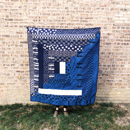 Ray Quilt by Carolyn Friedlander in navy, blue, and white geometric prints, displayed against brick wall