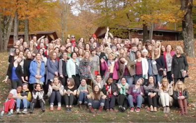 Large group photo of sewing retreat attendees gathered outdoors in the Catskills during fall, with trees in background