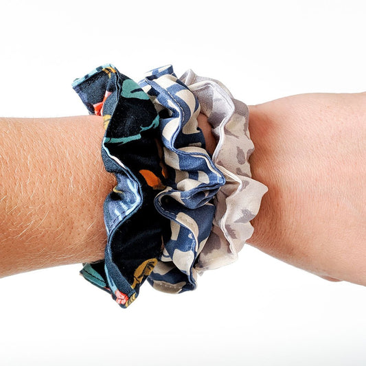 Three scrunchies made from fabric scraps in navy florals and neutral prints, worn stacked on a wrist