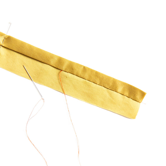 Fold of yellow fabric with needle and thread demonstrating slip stitch hand sewing technique