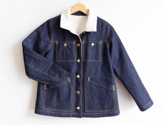 Thayer Jacket in dark denim with cream sherpa collar, brass buttons, four patch pockets, and yellow topstitching on hanger