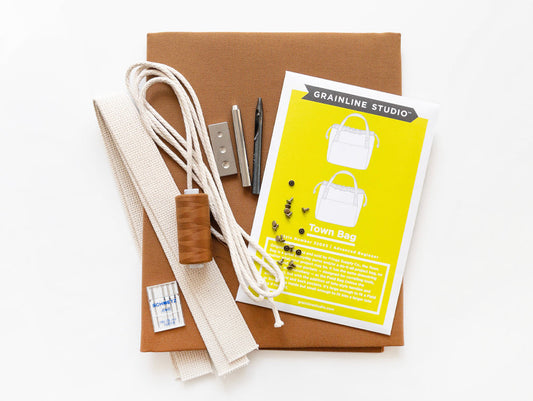 Grainline Studio Town Bag sewing supplies flatlay with toffee canvas, cream handles, drawstring, rivets, and pattern envelope