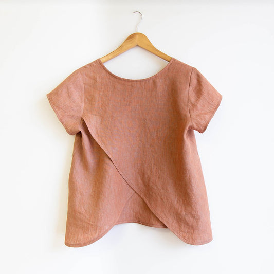 Scout Tee sewing pattern modification with split back detail in coral linen, showing crossover split seam on wooden hanger
