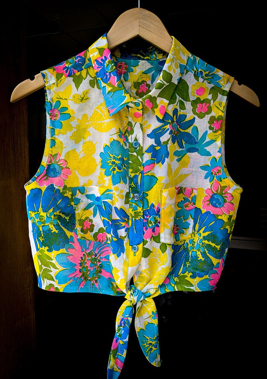 Sleeveless Alder Shirt in bold floral print, button-front with patch pockets and curved tie hem, on wooden hanger