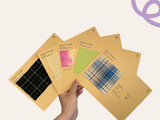 Hand holding five Yardblox fabric swatch cards showing dark plaid, gingham, tie-dye, green solid, and blue plaid textiles