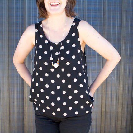 Person wearing a black and white polka dot silk tank top with V-neckline, pendant necklace, and black pants