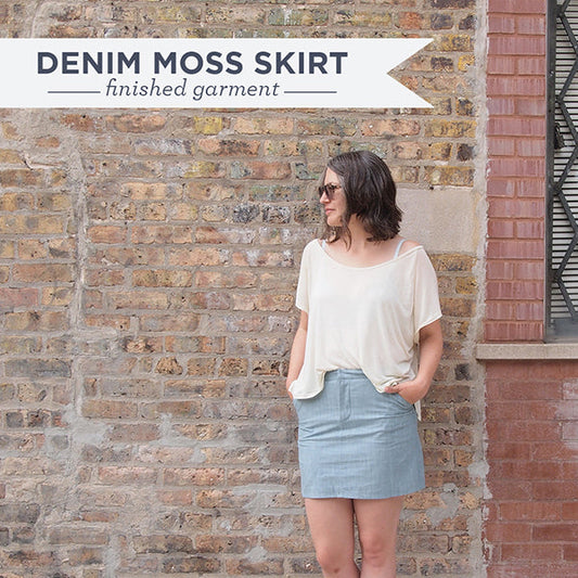 Denim Moss Skirt finished garment worn with cream top against brick wall, with Denim Moss Skirt finished garment text overlay