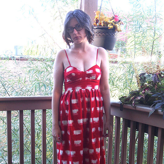 Woman wearing a red and white ikat sundress with sweetheart neckline, spaghetti straps, and gathered skirt on a deck