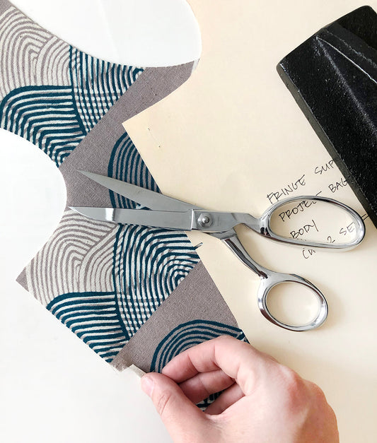 Snipped notch on Stowe Bag in wave print fabric with dressmaking scissors, oaktag pattern piece, and black pattern weight