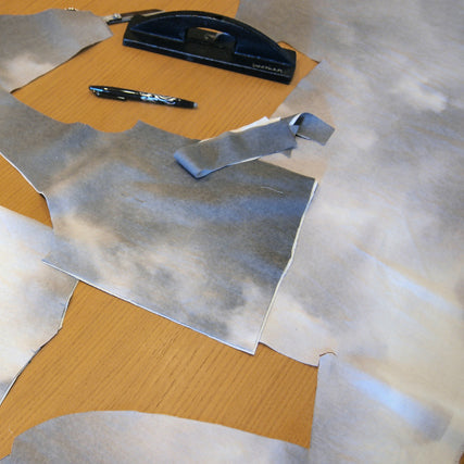 Cut cloud print fabric pieces laid out on a wooden table with a fabric marker and pattern weights