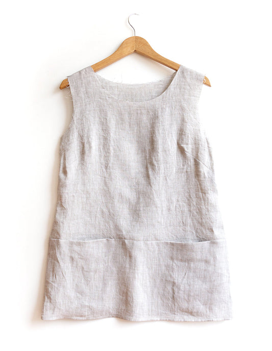 Uniform Tunic in natural linen with waistline seam, side seams sewn, neckline and armholes unfinished, on wooden hanger