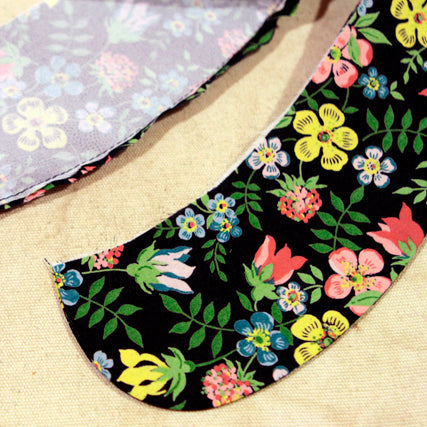 Two Peter Pan collar pieces in floral fabric showing trimmed and graded seam allowances on curved edges on a cream background