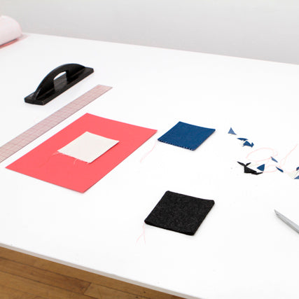 Corner-turning technique demo with coral, navy, and black fabric swatches, ruler, seam ripper, and clapper on a white table