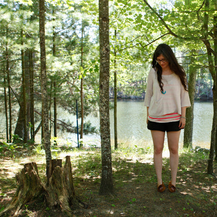 Person wearing Maritime Shorts in linen with a striped raglan tee, standing in a wooded area near a lake
