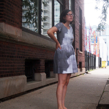Woman wearing a lavender cloud print short-sleeve A-line dress standing on an urban brick sidewalk