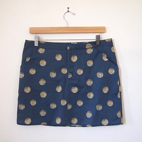 Moss Skirt in navy organic cotton sateen with gold polka dot print, hung on a wooden skirt hanger