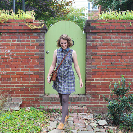 Person in blue plaid Alder Shirtdress with chambray collar, standing in front of a green arched door in a brick wall