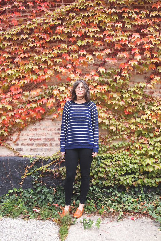 Person wearing navy and white striped Linden Sweatshirt with black pants against brick wall covered in red and orange fall ivy