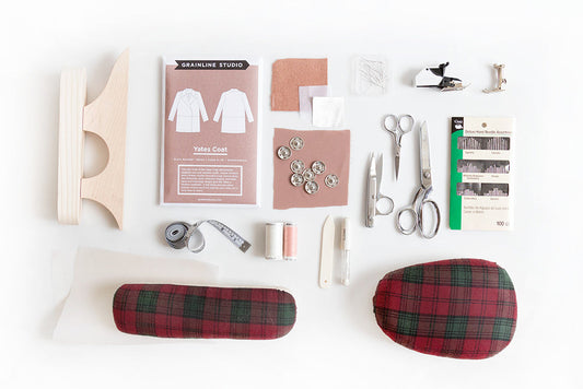 Yates Coat sewing supplies flat lay: pattern envelope, scissors, tape measure, thread, snaps, sleeve roll, and tailor's board