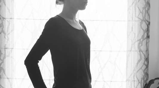 Black and white photo of person in long-sleeve Lark Tee in black silk knit, standing in profile against a bright window