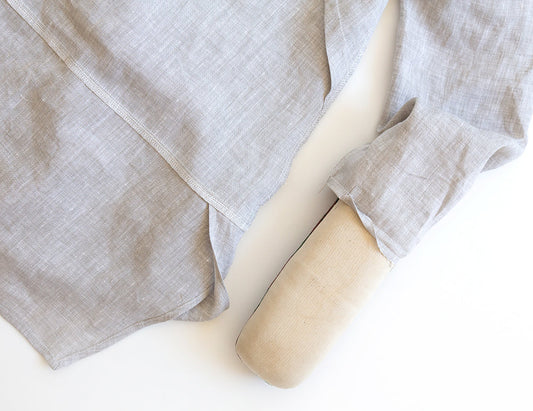 Uniform Tunic sleeve in natural linen being hemmed over a sleeve roll, showing serged underarm seam