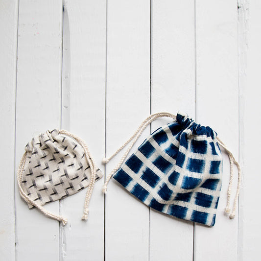 Two drawstring pouches on white shiplap: a small neutral woven print and a larger navy and white ikat plaid