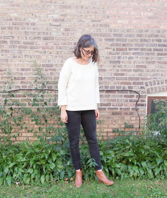 Hemlock Tee in ivory wool knit with three-quarter sleeves styled with dark skinny jeans and tan ankle boots against a brick wall