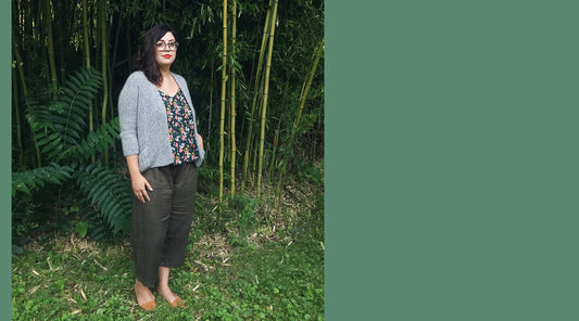 Person wearing gray cardigan over dark floral tank top and olive cropped pants, standing in front of bamboo