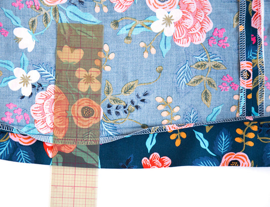 Farrow Dress hem tutorial showing folded fabric with serged edges, right and wrong side of navy floral print with clear ruler