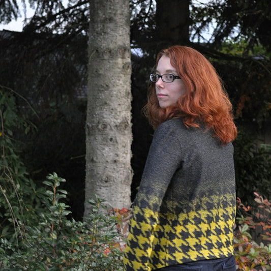 Person wearing Morris Blazer in charcoal and yellow houndstooth knit, photographed outdoors among evergreen trees