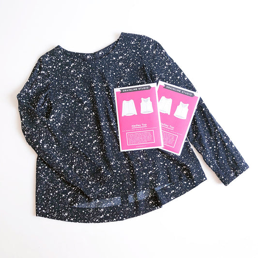 Hadley Top sewing pattern envelopes in hot pink displayed with navy speckled rayon woven fabric on white surface