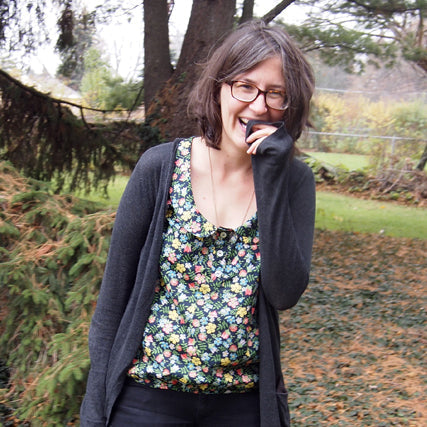 Person wearing a dark floral Liberty print top with a charcoal cardigan, laughing outdoors in an autumn garden setting