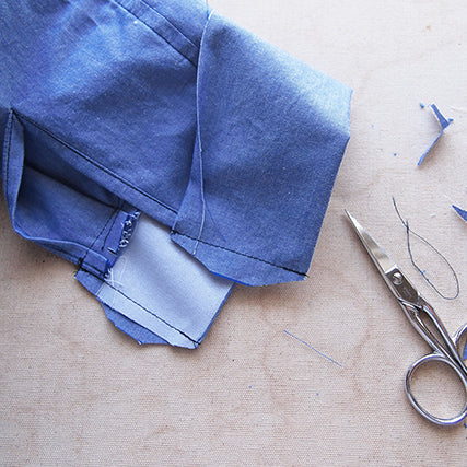 Close-up of a blue chambray Archer Button-Up cuff being attached to the sleeve, with scissors and clipped threads nearby