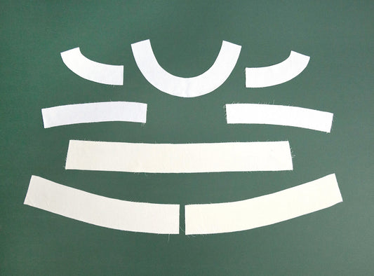 Hadley Top interfaced fabric pieces on green background: curved neckline facings, straight band, and curved hem facings