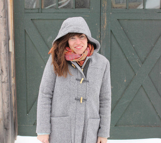Person in gray Cascade Duffle Coat with toggle closures and hood, styled with a red plaid scarf in front of green barn doors