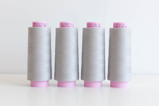 Four cones of Mettler Seracor light gray thread with pink labels, arranged in a row for serger sewing