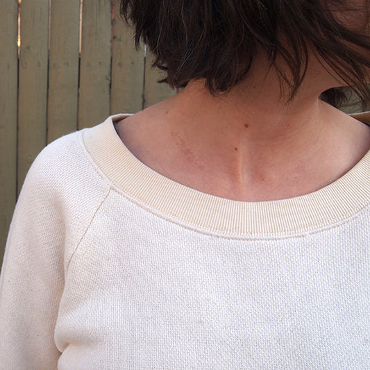 Close-up of cream french terry Linden Sweatshirt showing the ribbed neckband and raglan sleeve seam from the front