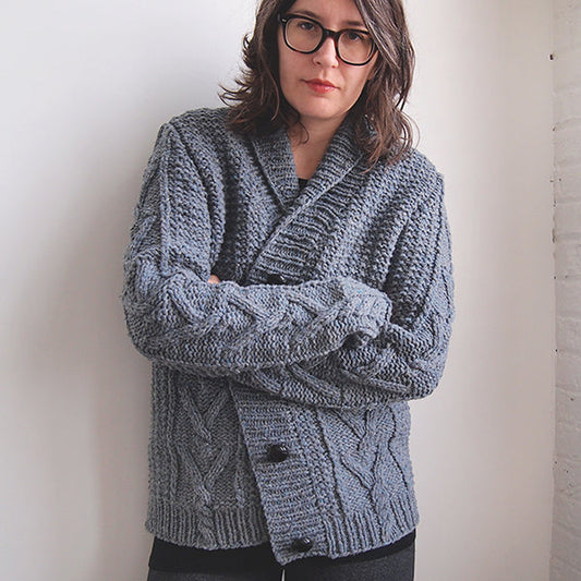 Woman wearing gray cable knit Bellows Cardigan by Michele Wang with shawl collar and button front, arms crossed