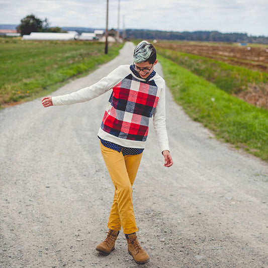 Linden Sweatshirt in red plaid colorblock with white sleeves, worn with mustard pants and boots on a rural road