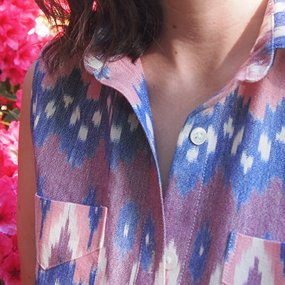 Close-up of a sleeveless Archer Button-Up in pink and blue ikat print showing the collar, white button, and patch pocket