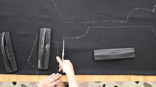 Hands cutting black fabric with chalk-marked Archer Button Up pattern pieces and notches, with pattern weights on top