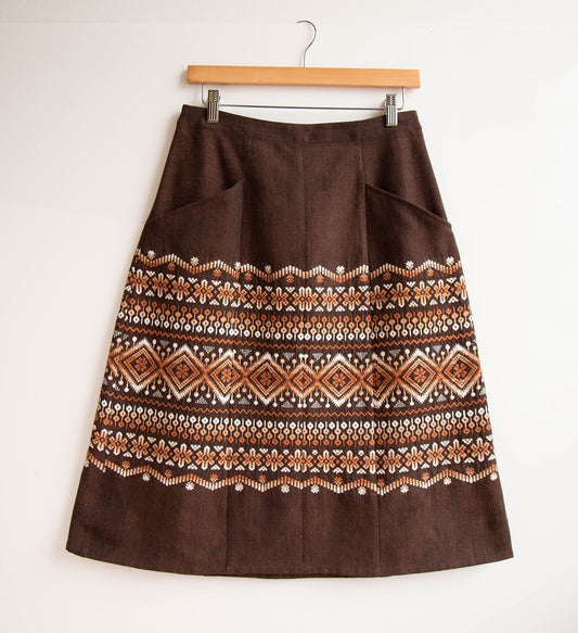 Reed Skirt in dark brown linen with geometric embroidered border in rust and white, patch pockets, on wooden hanger