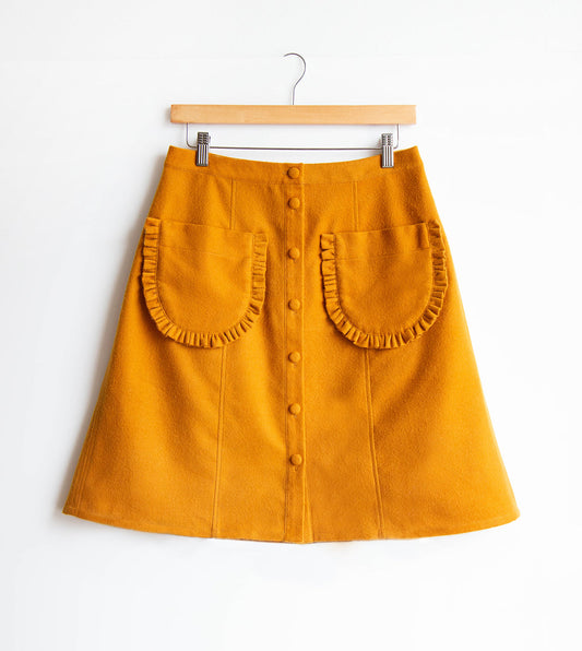 Reed Skirt in golden yellow wool with button-front placket, ruffled patch pockets, and A-line silhouette on wooden hanger
