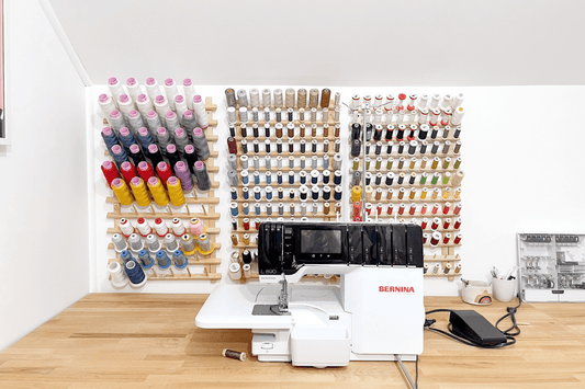 BERNINA L890 serger on wood desk with three wooden wall-mounted thread racks displaying colorful spools organized by color