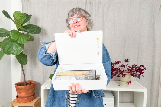 Jen Beeman in denim shirt holding open white storage box full of knitting needles, plants in background, Making Space to Make