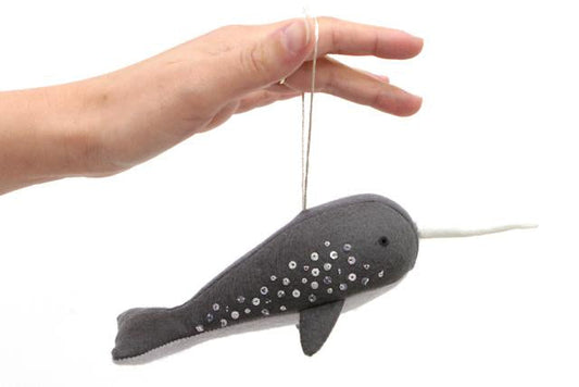 Hand holding gray felt narwhal ornament with sequin embellishments and white silk tusk, suspended by thread