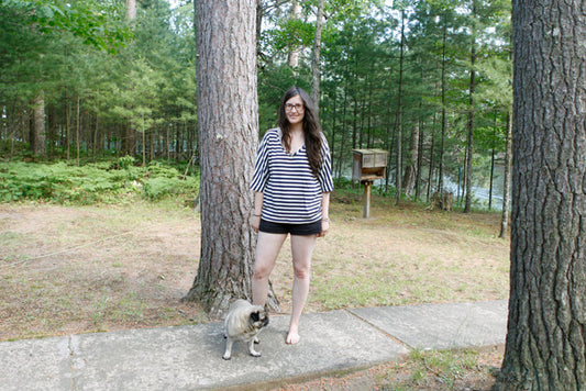 Person wearing navy and white striped Seafaring Sweater with kimono sleeves in a forest setting by a lake with a pug